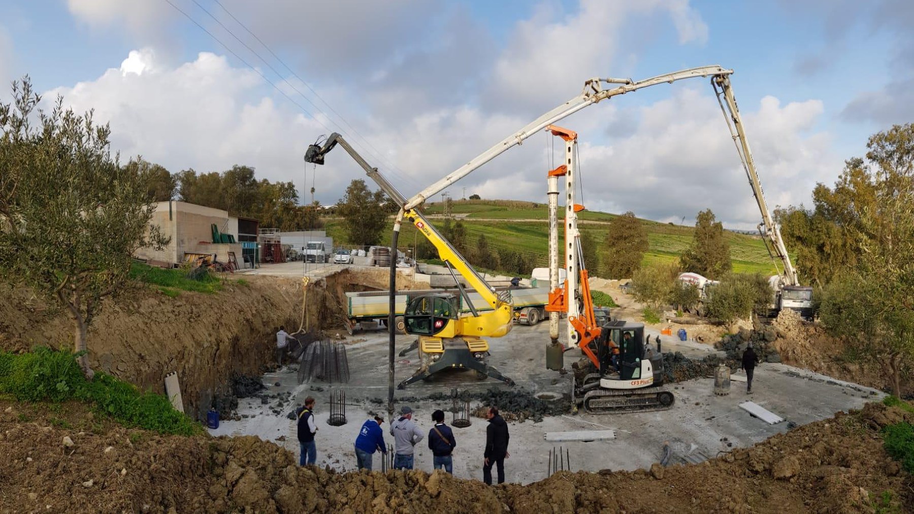 Cantiere con mezzi per fondazioni, pompa per calcestruzzo e personale al lavoro